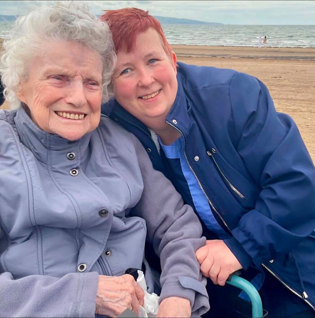 an older lady and a carer posing for a photo by the beach